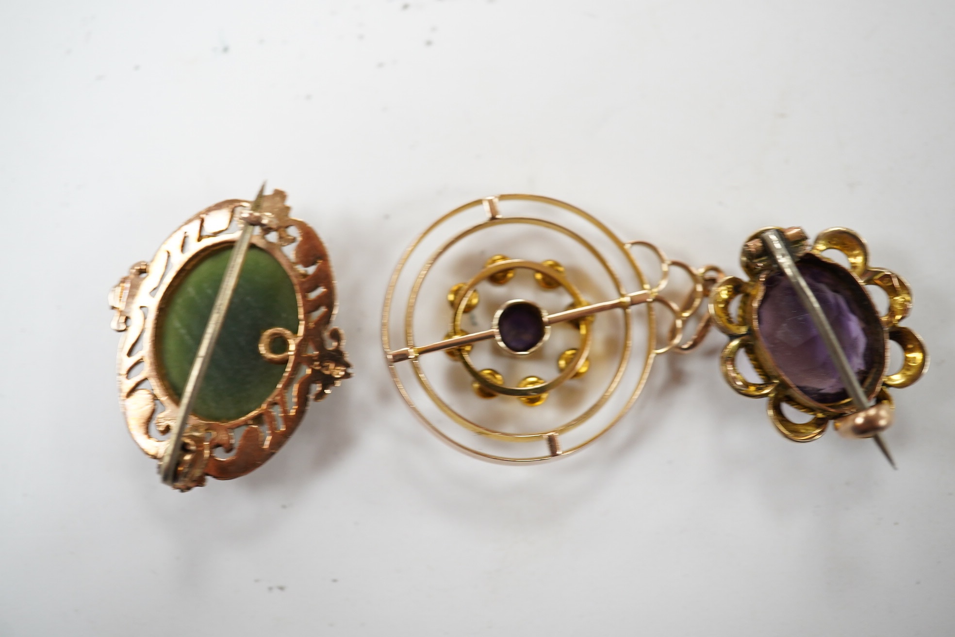 An Edwardian 9ct, sapphire and seed pearl cluster set open work circular pendant, 26mm, together with a similar 9ct, amethyst and seed pearl set brooch and a 9ct and nephrite set brooch, gross weight 7.4 grams. Condition